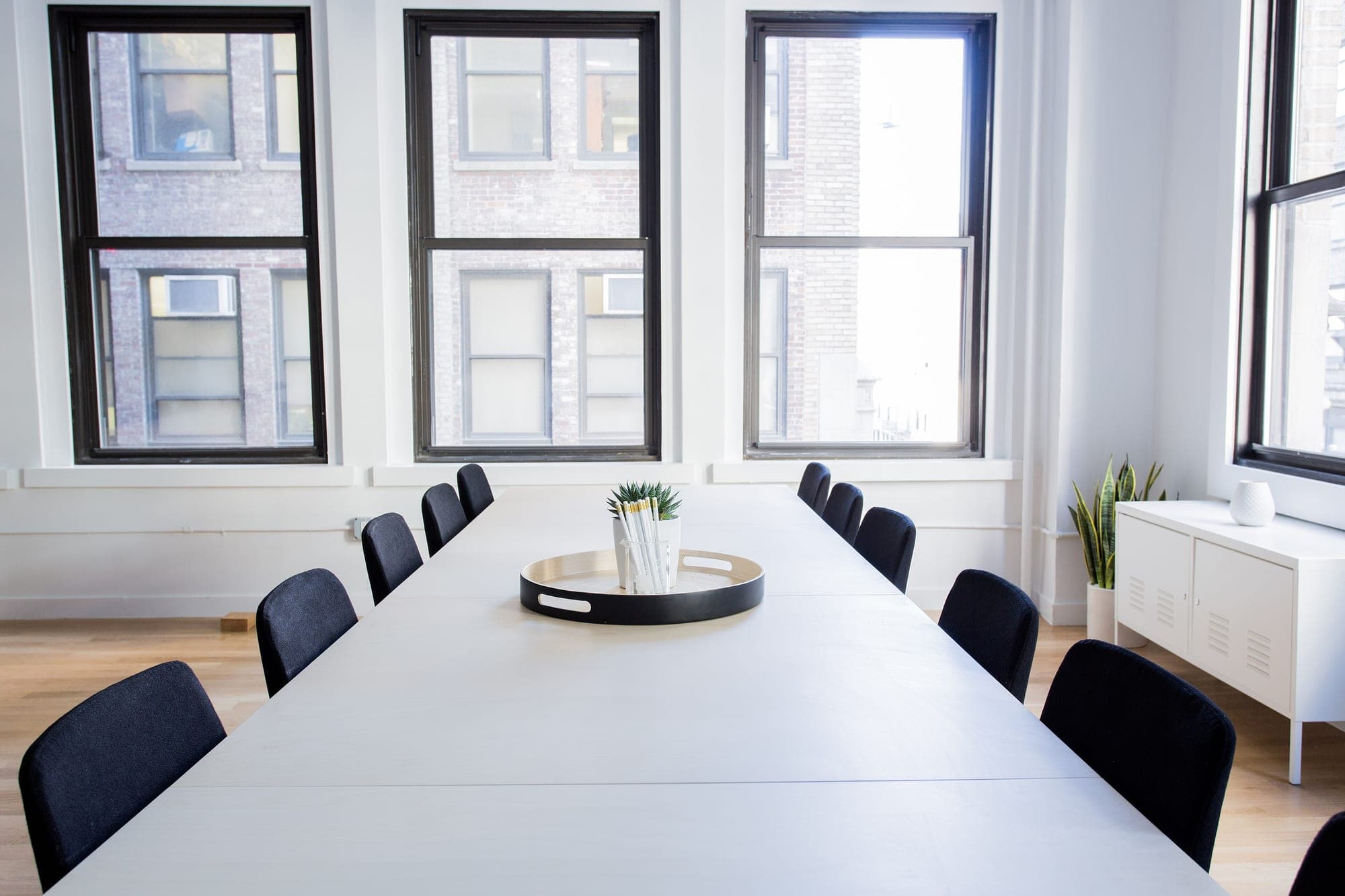 A long white table under tall windows, 16 chairs and nobody in the room
