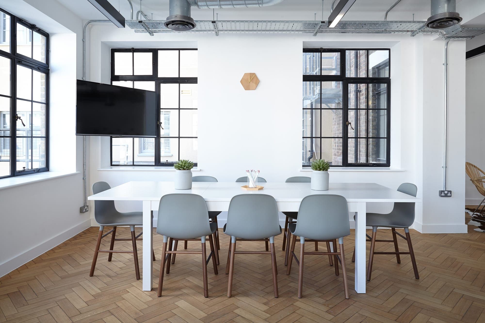 A white meeting table under 2 tall windows on a herringbone floor